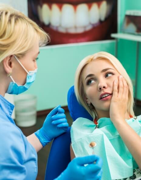 Woman holding her cheek while talking to emergency dentist