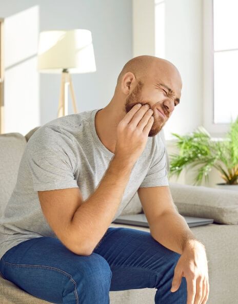 Man sitting on couch holding his cheek in pain