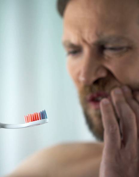 Man touching his cheek looking at a red toothbrush from bleeding gums in Arlington