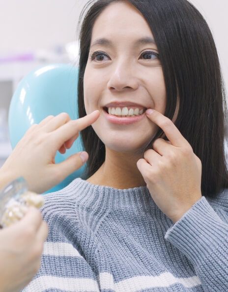 Woman in dental chair pointing to her smile