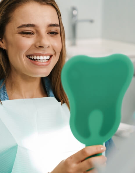 Young woman in dental chair looking at smile in mirror