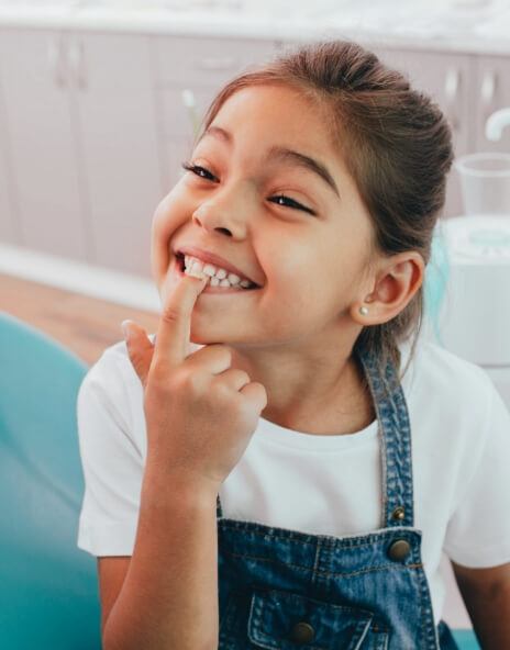 Young girl in dental chair pointing to her teeth