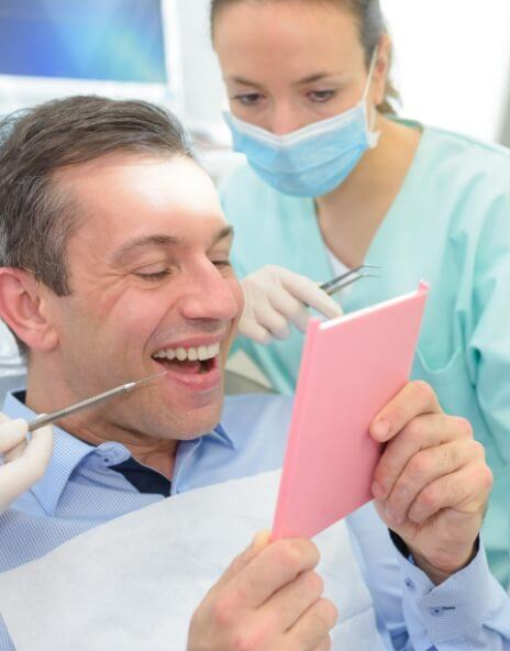 Man in dental chair admiring his smile in mirror