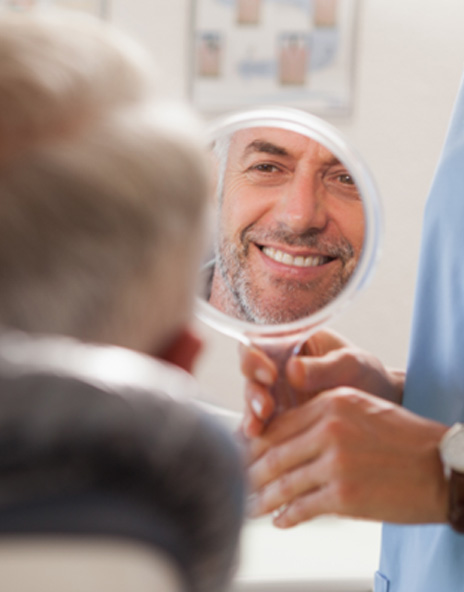 Man smiling at reflection in handheld mirror